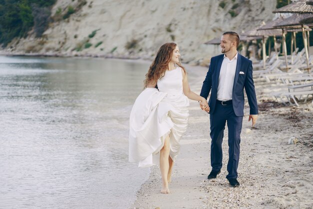 belle jeune mariée aux cheveux longs en robe blanche avec son jeune mari sur la plage