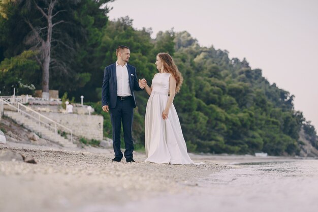 belle jeune mariée aux cheveux longs en robe blanche avec son jeune mari sur la plage