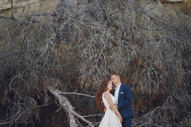 belle jeune mariée aux cheveux longs en robe blanche avec son jeune mari près des branches