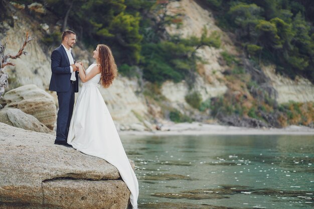 belle jeune mariée aux cheveux longs en robe blanche avec son jeune mari près de la rivière