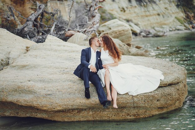 belle jeune mariée aux cheveux longs en robe blanche avec son jeune mari près de la rivière