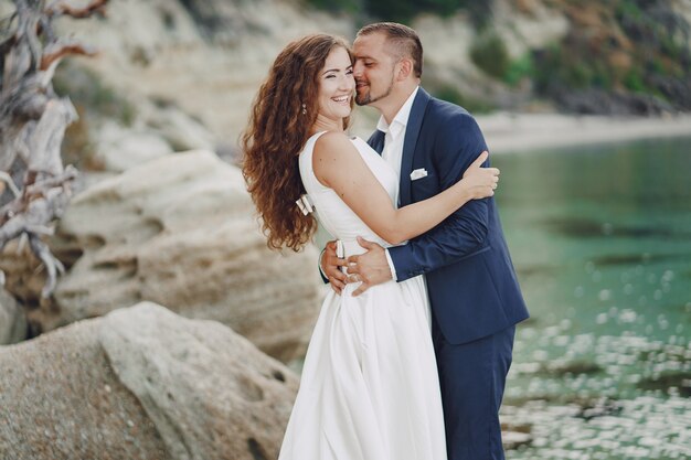 belle jeune mariée aux cheveux longs en robe blanche avec son jeune mari près de la rivière