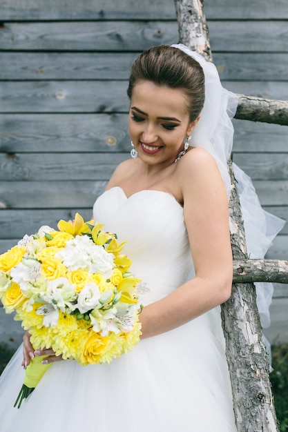 Belle jeune mariée avec bouquet est debout à l'échelle