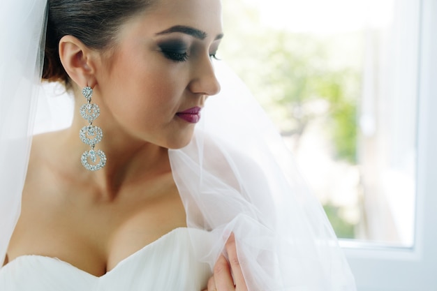 Belle jeune mariée posant contre la fenêtre dans la chambre d'hôtel