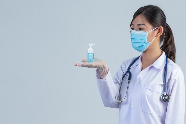 Belle jeune médecin porte un masque tout en tenant le gel des mains sur le mur gris.