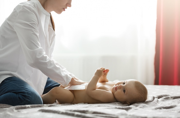 Photo gratuit belle jeune mère en chemise blanche et jeans mettant la couche sur le bébé nouveau-né mignon se préparant pour le dîner de famille avec les grands-parents. passer du temps spécial en famille.