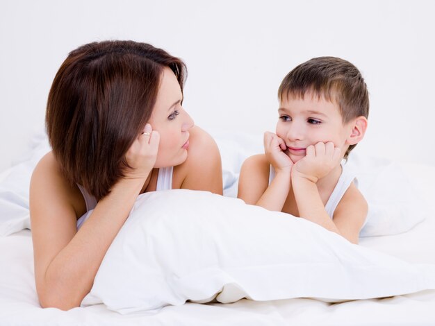 Belle jeune mère et le fils se regardent allongé dans un lit