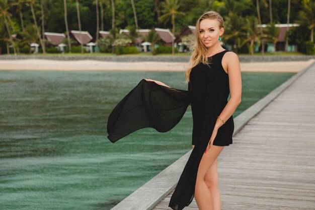 Belle jolie femme vêtue d'une robe noire posant sur la jetée dans un hôtel de luxe, vacances d'été, plage tropicale