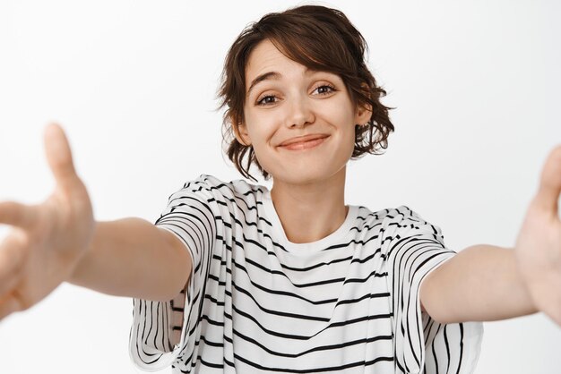 Belle jolie fille brune atteignant un câlin recevoir quelque chose dans les mains tendues ouvertes et souriant tendrement debout sur fond blanc