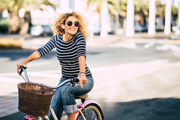 Belle et joyeuse jeune femme adulte profite d'une balade à vélo dans une activité de loisirs de plein air urbaine ensoleillée dans la ville - portrait de gens heureux - femme branchée à l'extérieur s'amusant