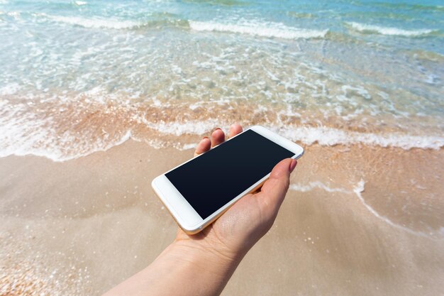Belle main de femme à l'aide d'un téléphone intelligent à la plage