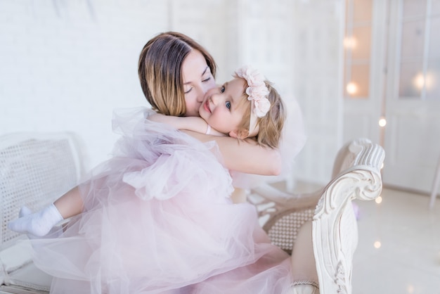 Belle maman et fille embrassent mutuellement tendre assis sur une chaise blanche