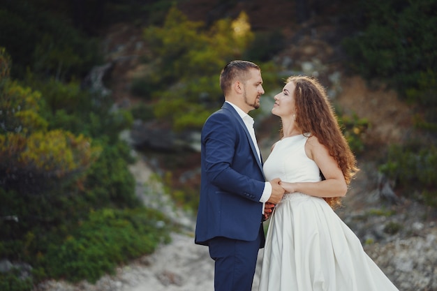 belle mariée aux cheveux longs en robe blanche avec son jeune homme marchant dans la nature