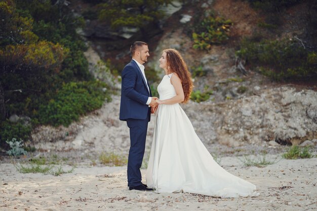 belle mariée aux cheveux longs en robe blanche avec son jeune homme marchant dans la nature