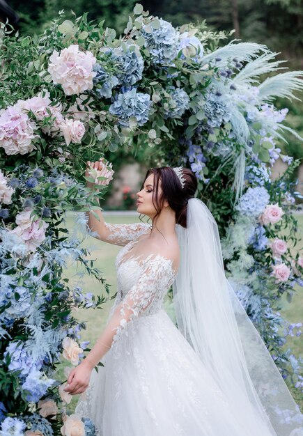 Belle mariée brune caucasienne est debout près de la voûte faite d'hortensia bleu et rose à l'extérieur