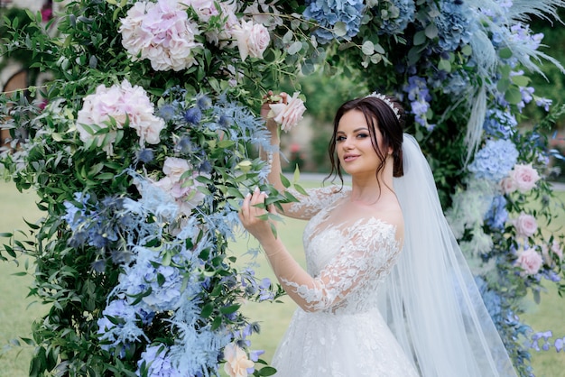 Belle mariée brune près de l'arcade en hortensia bleu et ruscus, jour du mariage