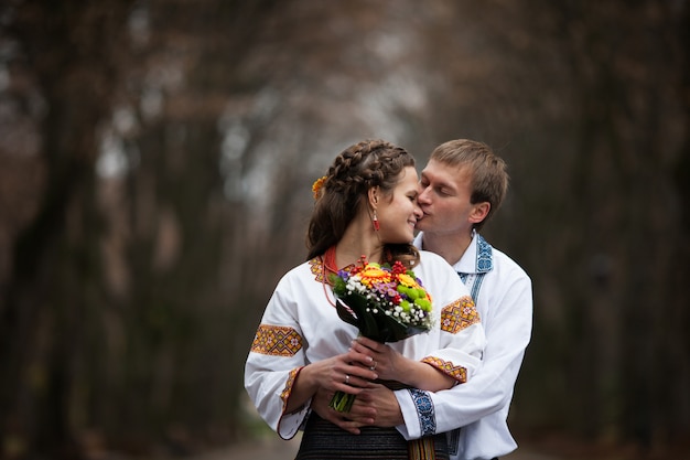 Belle mariée et mariée ukrainienne en costumes de broderie indigènes sur le fond des arbres dans un parc, cérémonie de mariage traditionnelle