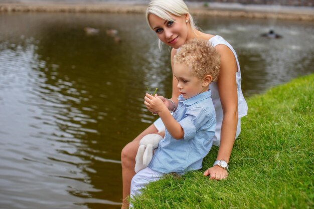 Belle mère avec son enfant assis sur l'herbe près de la rivière.