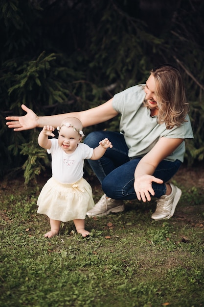 Belle petite fille aux cheveux courts et blonds et joli sourire en robe blanche est assise sur une herbe dans le parc en été avec sa mère