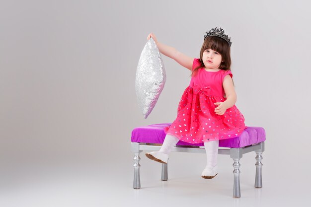 Belle Petite Fille Brune En Robe De Princesse Rose Avec Couronne Assise Sur Une Chaise Rose Et Jouant Avec Un Oreiller Bebe Mignon Photo Premium