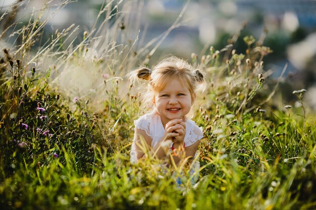 Belle petite fille en chemise blanche et jeans est assis sur la pelouse avec un grand paysage