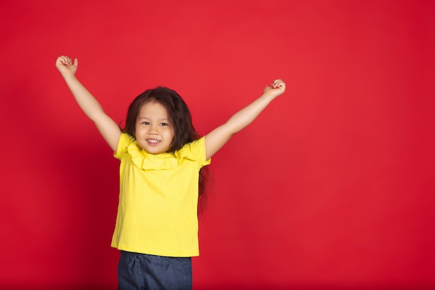 Belle petite fille émotionnelle isolée sur l'espace rouge. Portrait demi-longueur d'enfant heureux montrant un geste et pointant vers le haut. Concept d'expression faciale, émotions humaines, enfance.