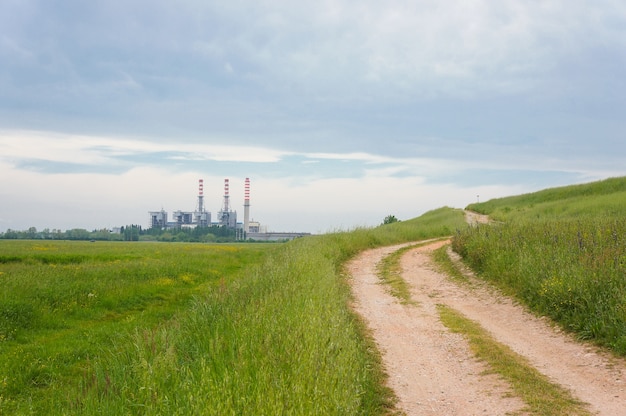 Belle photo d'un champ vert sur le côté d'un chemin de terre avec un bâtiment et un ciel nuageux