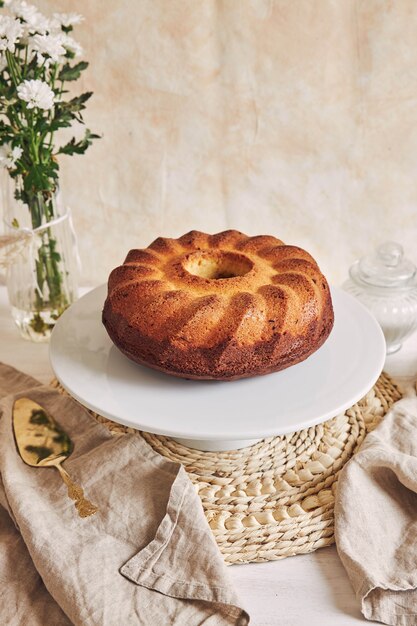 Belle photo d'un délicieux gâteau à l'anneau posé sur une assiette blanche et une fleur blanche à proximité