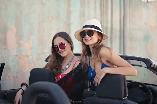 Belle photo de deux amies avec des accessoires sur une voiture de sport décapotable