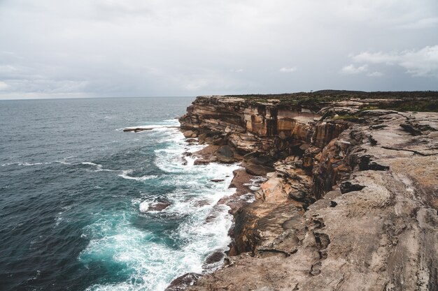 Belle photo d'une grande falaise à côté de l'eau bleue un jour sombre