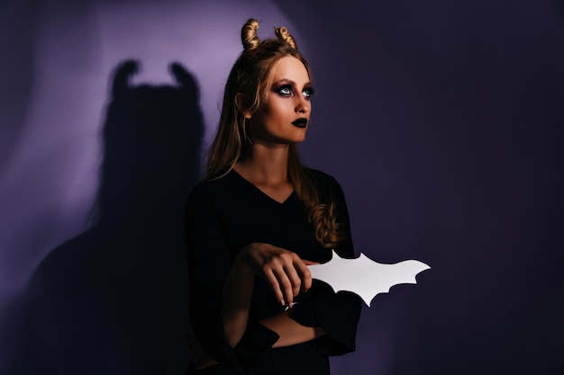 Belle sorcière debout sur un mur sombre et levant les yeux. incroyable fille blonde se préparant à l'événement d'halloween.