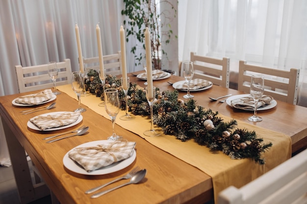 Belle table de service de Noël avec bougies et décoration de sapin en gros plan intérieur moderne et confortable. Célébration des vacances de décembre nouvel an entouré de verres et assiettes décorés de saison