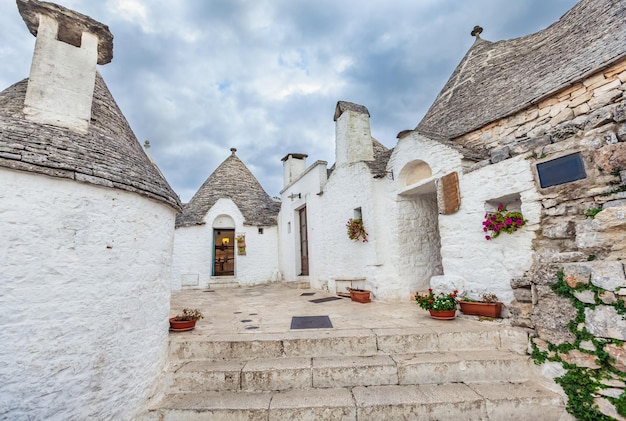 Belle ville d'Alberobello avec des maisons Trulli parmi les plantes vertes et les fleurs, principal quartier touristique, région des Pouilles, Italie du Sud. Bâtiments blanchis à la chaux typiques construits avec des murs en pierres sèches et