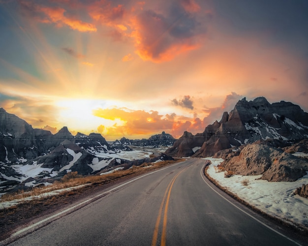 Belle vue sur une étroite route de campagne avec des montagnes rocheuses couvertes de neige au loin