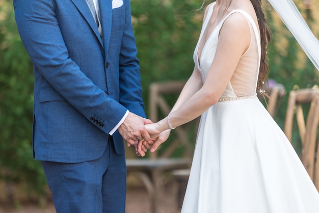 Belle vue sur la mariée romantique et le marié se tenant la main lors de leur mariage