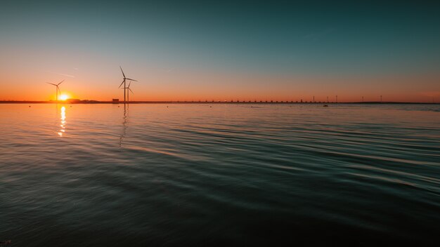 Belle vue sur l'océan calme avec des turbines sous le coucher de soleil fascinant dans le