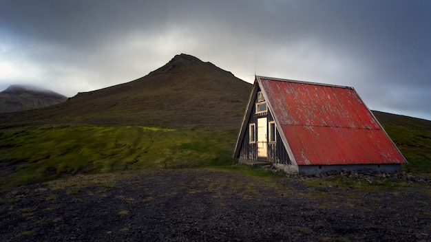 Belle vue sur une vieille maison rouge isolée au milieu d'un champ vert à côté des montagnes
