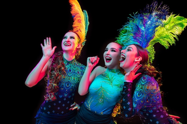 Belles jeunes femmes en carnaval, costume de mascarade élégant avec des plumes sur fond noir en néon.