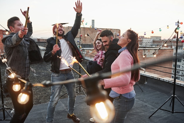 De belles personnes. Jouer avec des cierges magiques sur le toit. Groupe de jeunes beaux amis