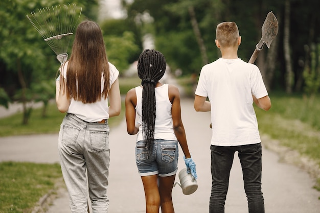 Photo gratuite bénévoles travaillant dans le parc. trois adolescents vont planter un arbre. portant râteaux, arrosoir et semis. des gens divers.