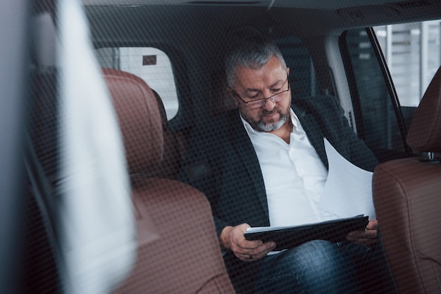 Besoin d'attention aux détails. Documents sur le siège arrière de la voiture. Homme d'affaires senior avec documents