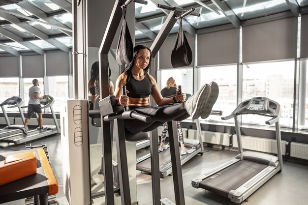 Le bien-être. Jeune femme caucasienne musclée pratiquant dans une salle de sport avec équipement. Modèle féminin athlétique faisant des exercices ABS, entraînant le haut du corps, le ventre. Bien-être, mode de vie sain, musculation.