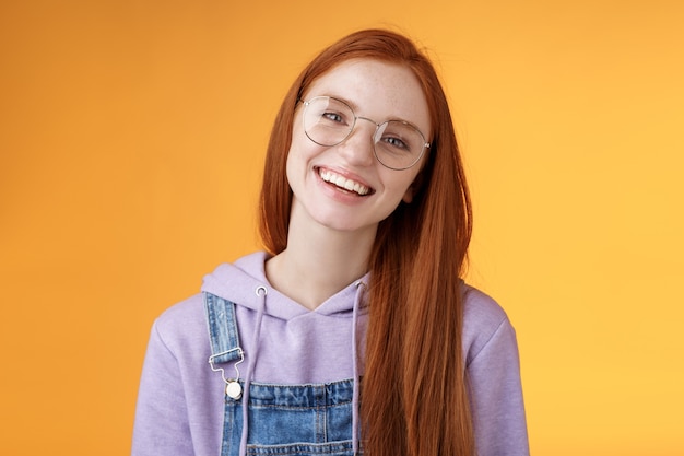 Bien-être, mode de vie, concept de personnes. Jolie jeune fille rousse souriante à l'allure amicale et droite de longs cheveux roux naturel portant des lunettes riant joyeusement profiter d'une belle atmosphère de café relaxante