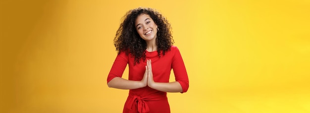 Bienvenue à l'intérieur du portrait d'une hôtesse sympathique et polie en robe rouge avec des cheveux bouclés