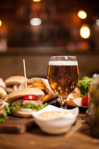 Bière dorée à côté de délicieux hamburgers sur table en bois. Frites. Salade verte. Frites. Sauce à l'ail.