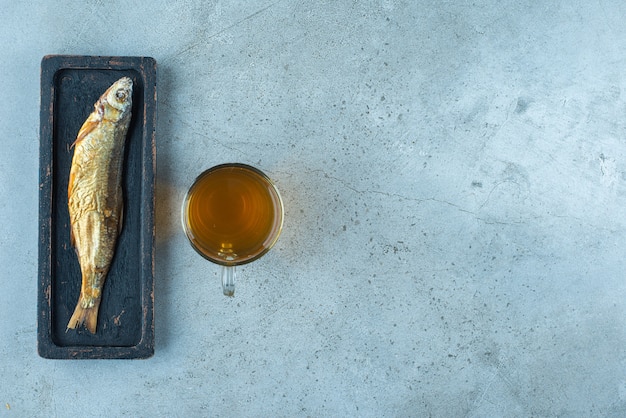 Une bière en verre à côté du poisson sur une assiette en bois, sur la table bleue.