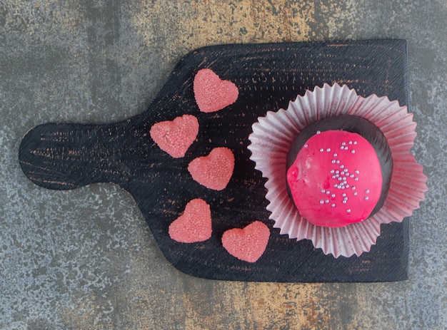 Biscuit au chocolat avec glaçage rose et bonbons sur planche de bois