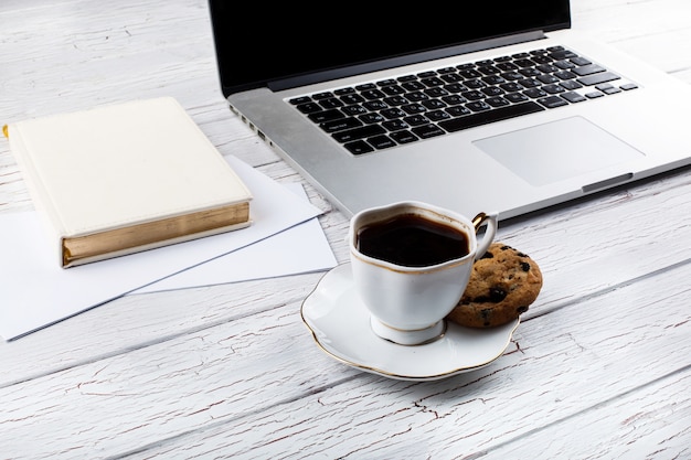 Photo gratuite biscuit au chocolat se trouve sur la palte de tasse de café blanc avant un ordinateur portable