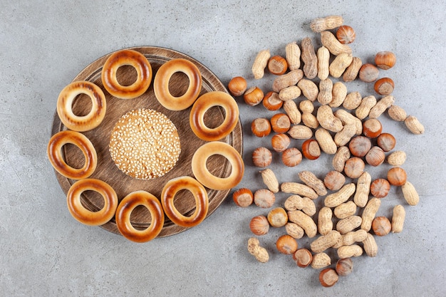 Photo gratuite biscuit unique entouré de sushki sur une planche de bois à côté d'un assortiment de noix éparpillés sur une surface en marbre.