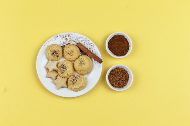 Biscuits sur une assiette avec café, bâton de cannelle sur fond jaune